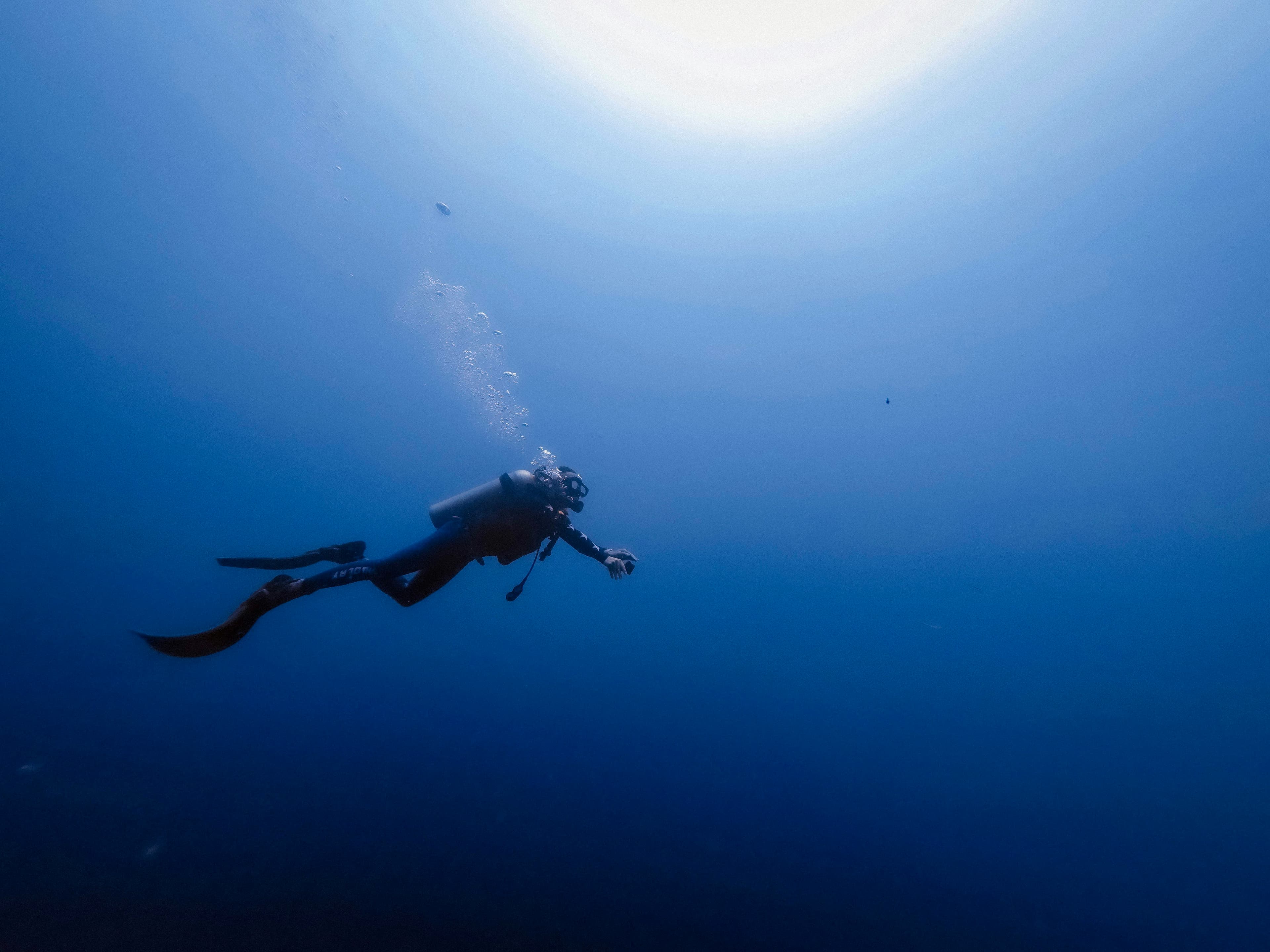 Scuba diver descending into deep blue ocean with sunlight rays filtering through water